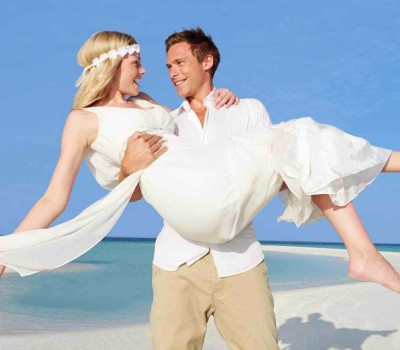 groom carries bride at beach